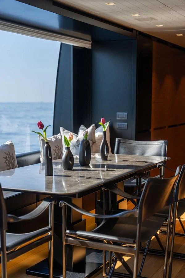The yacht's dining area features a sleek table with modern chairs, complemented by a stunning ocean view through large windows. aboard JACKI 8 Yacht for Sale