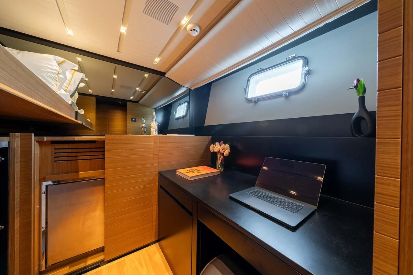 A cozy cabin featuring a work desk, a laptop, and a comfortable bed with modern lighting. aboard JACKI 8 Yacht for Sale