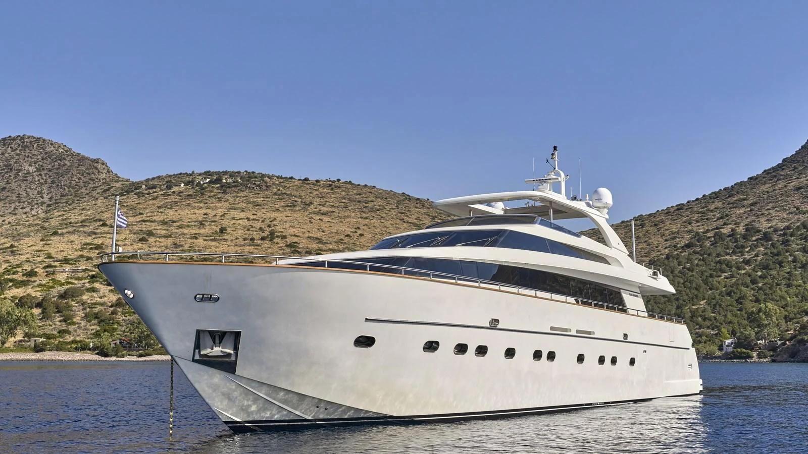 A sleek and modern yacht is anchored in a serene bay with a backdrop of rolling hills. aboard OASIS Yacht for Sale