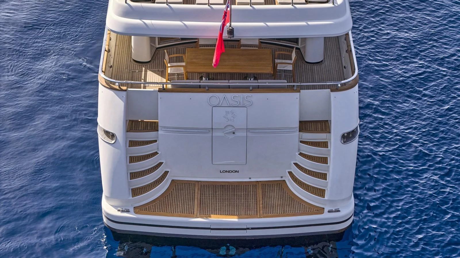 The yacht's aft deck features a spacious area with elegant wooden flooring and a dining table, perfect for alfresco dining. aboard OASIS Yacht for Sale