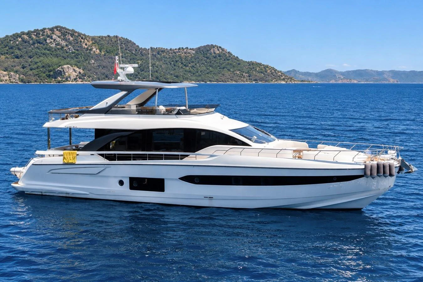 A sleek, modern yacht cruising on clear blue waters with scenic hills in the background. aboard MILES Yacht for Sale