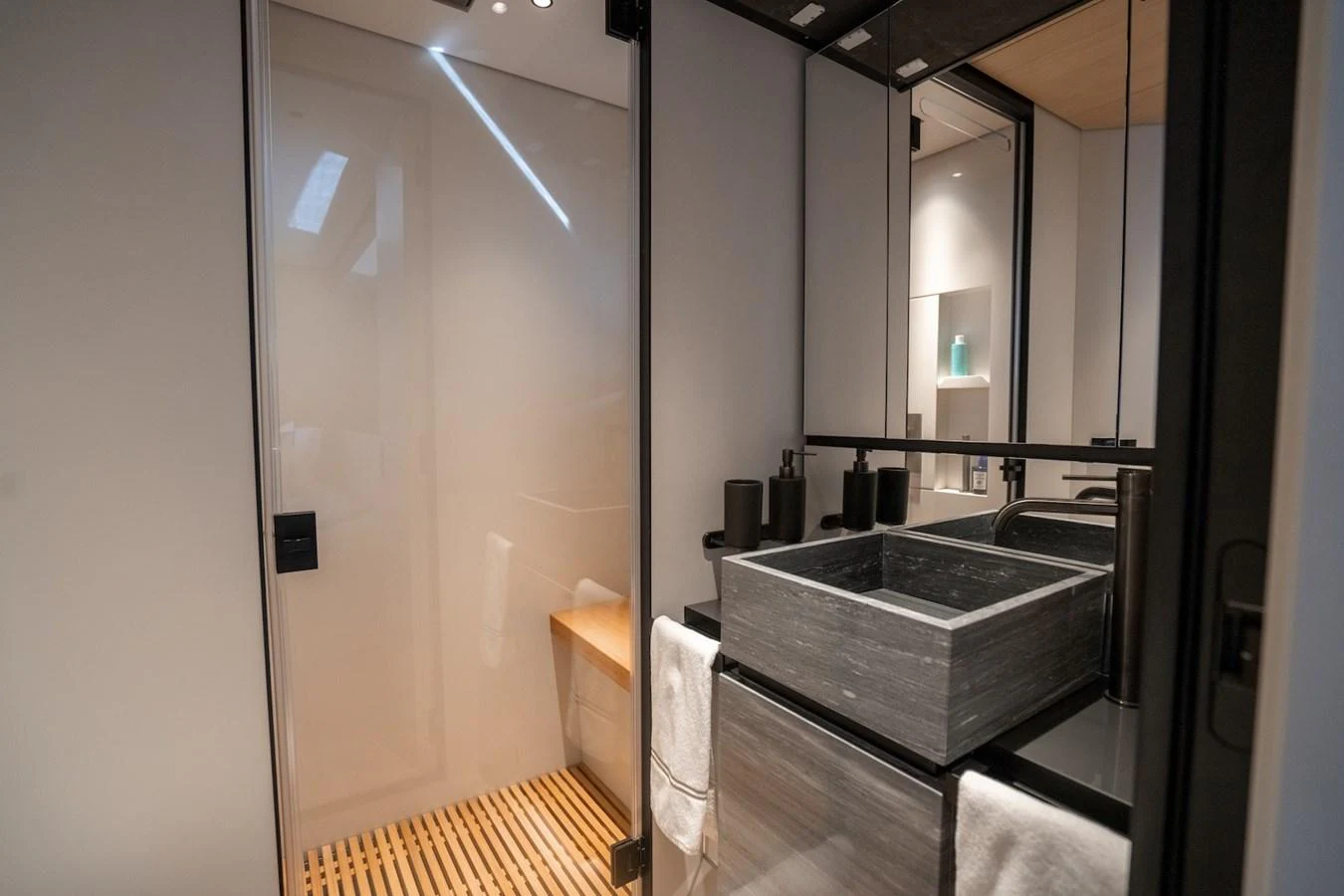A modern yacht bathroom featuring a sleek stone sink and a wooden slatted shower floor. aboard COME TOGETHER Yacht for Sale