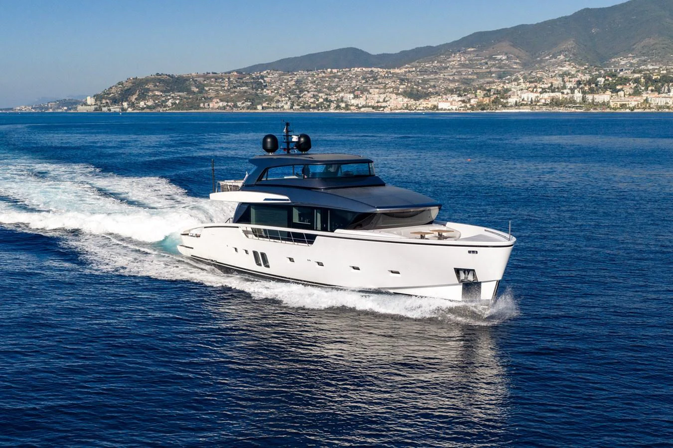 A sleek and modern yacht cruises through calm waters with a scenic coastal backdrop. aboard JUNIOR Yacht for Sale