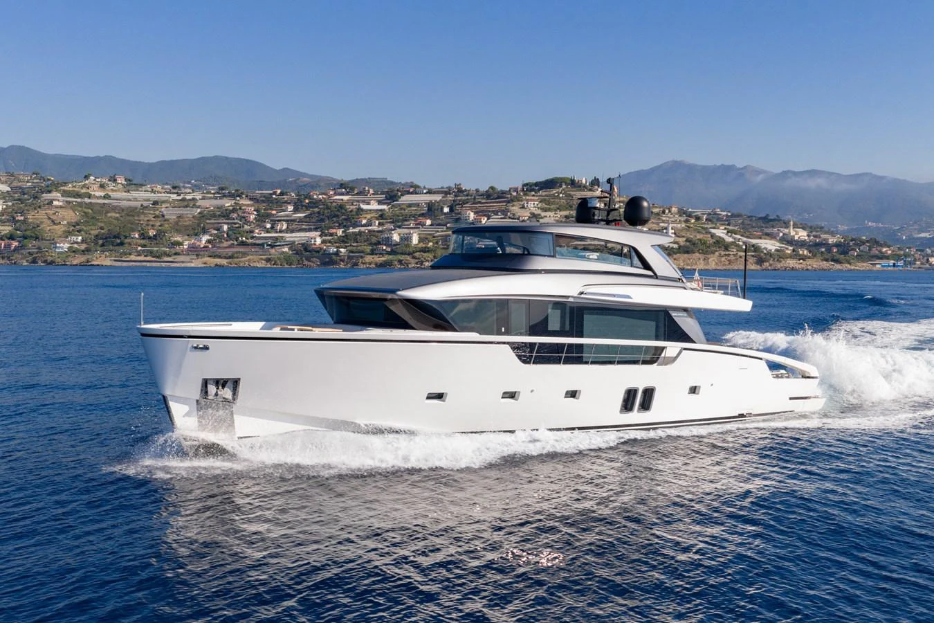 A sleek, modern yacht cruises through calm waters with a scenic coastal backdrop. aboard JUNIOR Yacht for Sale