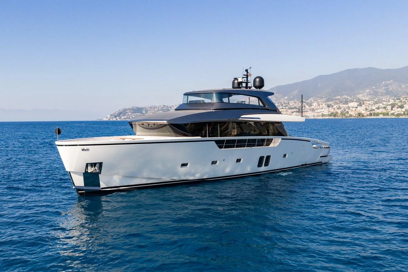 A sleek and modern yacht glides gracefully on the calm blue waters near a coastal town. aboard JUNIOR Yacht for Sale