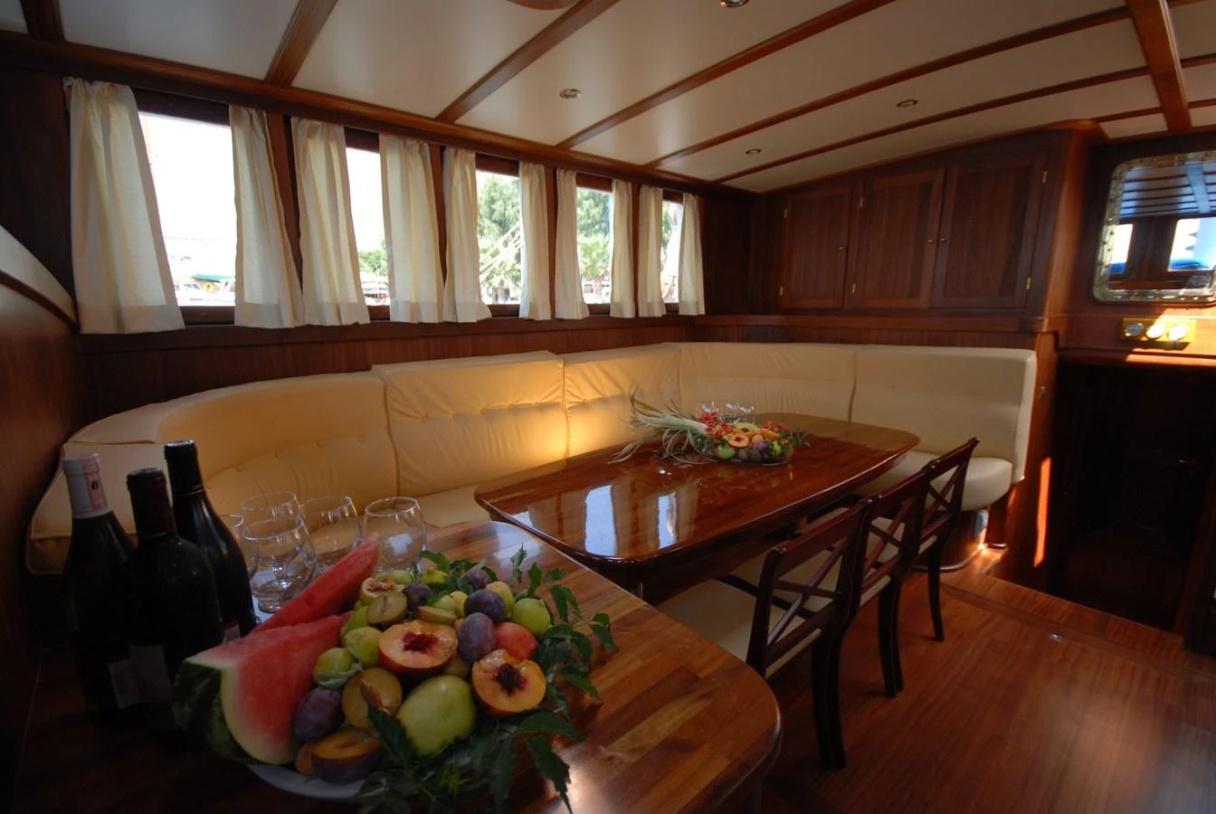 The yacht's dining area features a cozy seating arrangement with a wooden table and ample natural light. aboard ARINNA Yacht for Sale