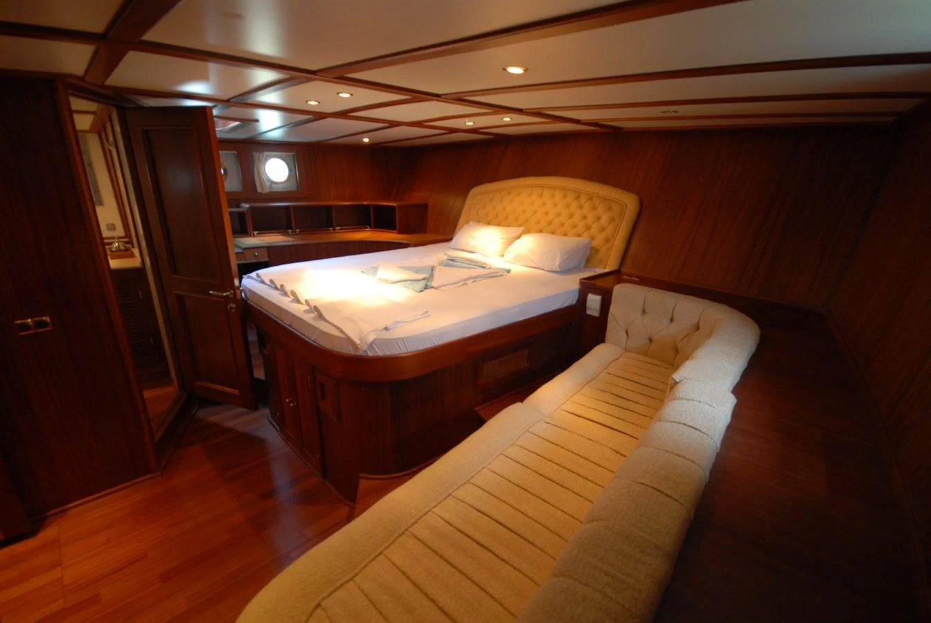 The stateroom features a luxurious bed with elegant wood paneling and a cozy seating area. aboard ARINNA Yacht for Sale