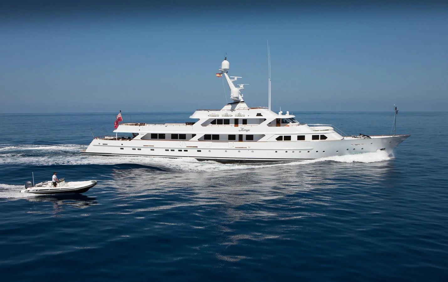 A luxurious white yacht cruises smoothly on the open sea, accompanied by a small tender boat. aboard MIRAGE Yacht for Sale