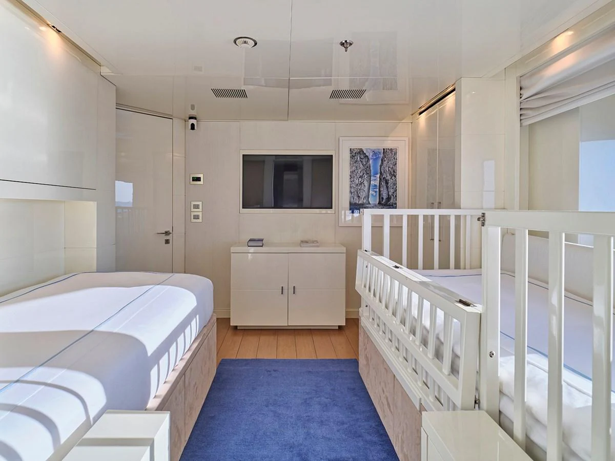 A serene twin stateroom featuring two single beds and a crib, with modern furnishings and a calming color palette. aboard BELITA Yacht for Sale