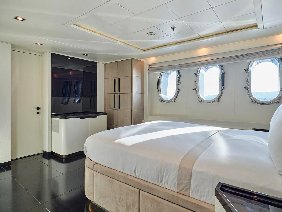 The stateroom features a luxurious bed with ample natural light from the porthole windows. aboard BELITA Yacht for Sale