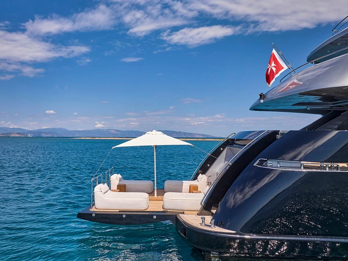 A luxurious yacht features an inviting aft deck with plush seating and a sunshade, set against a stunning ocean backdrop. aboard BELITA Yacht for Sale
