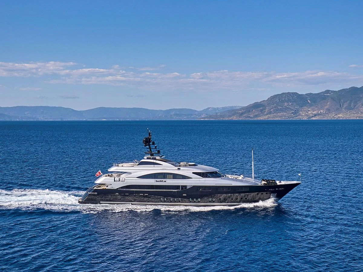 A sleek and modern yacht cruises through calm blue waters with a stunning backdrop of distant mountains. aboard BELITA Yacht for Sale