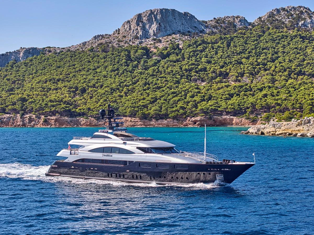A sleek and luxurious yacht cruises along a scenic coastline with lush greenery and rocky cliffs. aboard BELITA Yacht for Sale