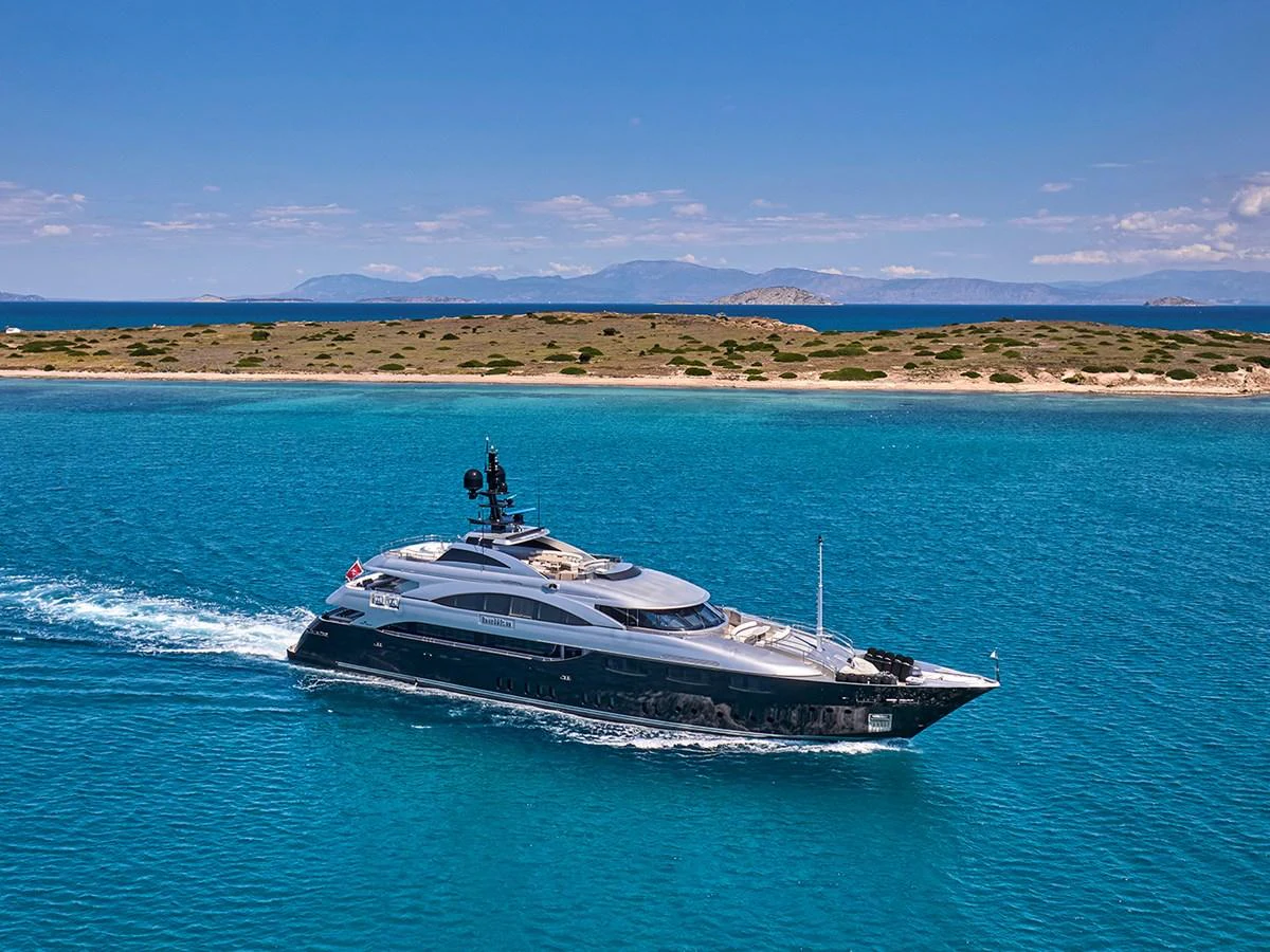 A sleek yacht cruises through clear blue waters with a scenic island backdrop. aboard BELITA Yacht for Sale