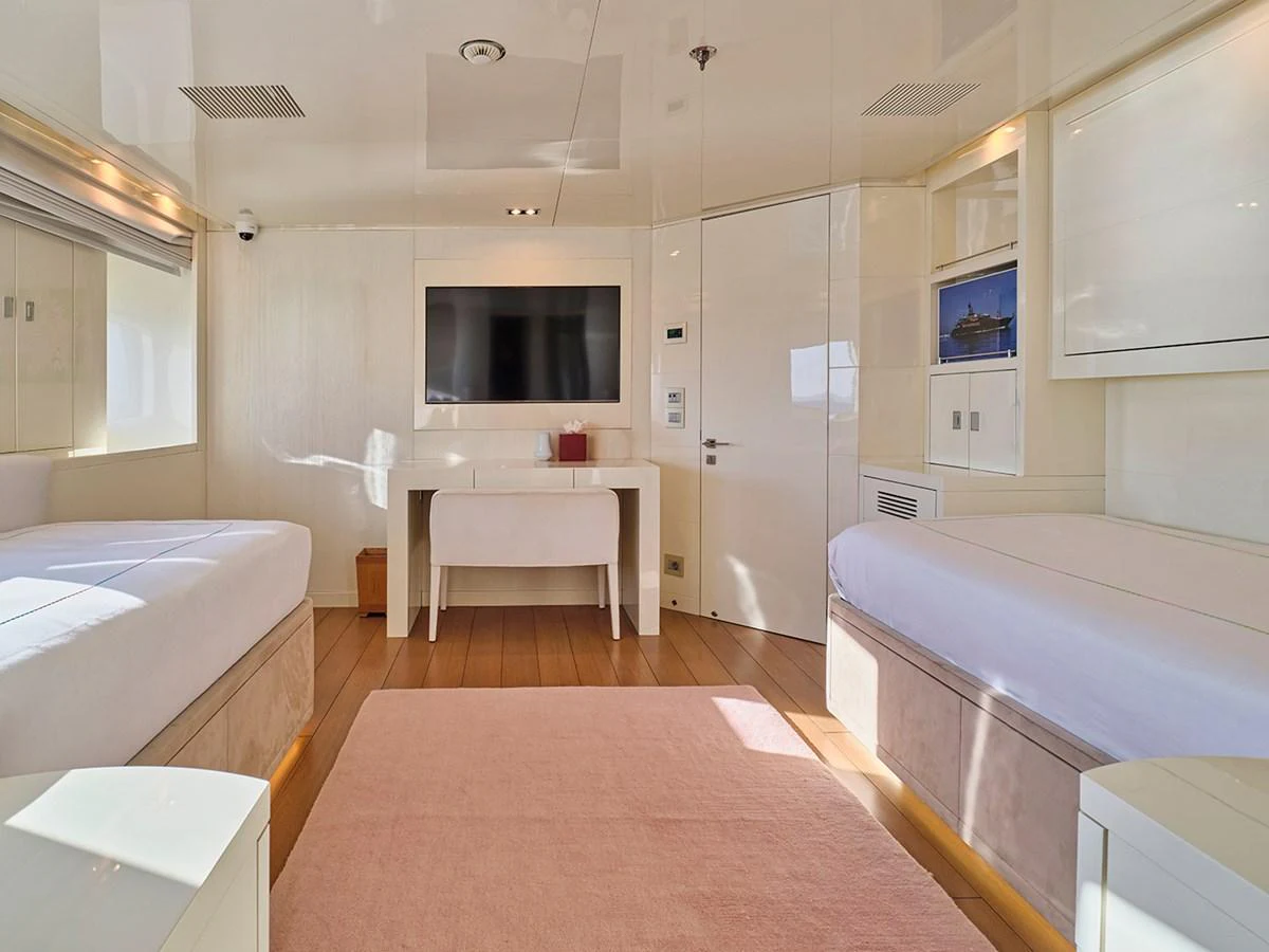 The guest cabin features twin beds, a wall-mounted TV, and a minimalist design with soft lighting. aboard BELITA Yacht for Sale