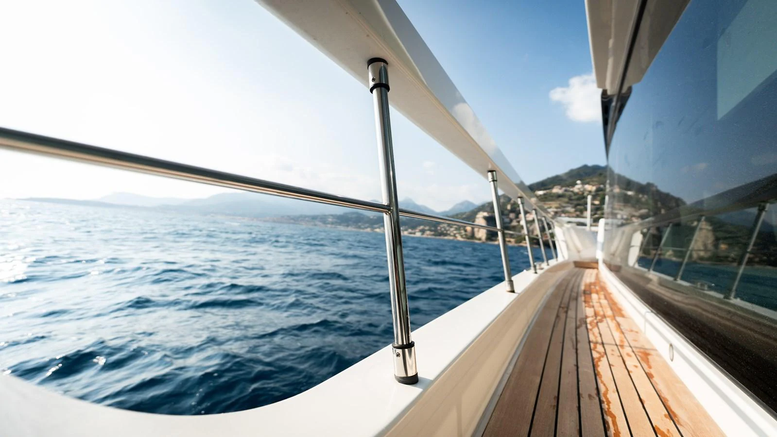 A sleek yacht cruising along the coastline with a view of the sea and distant hills. aboard LA Yacht for Sale