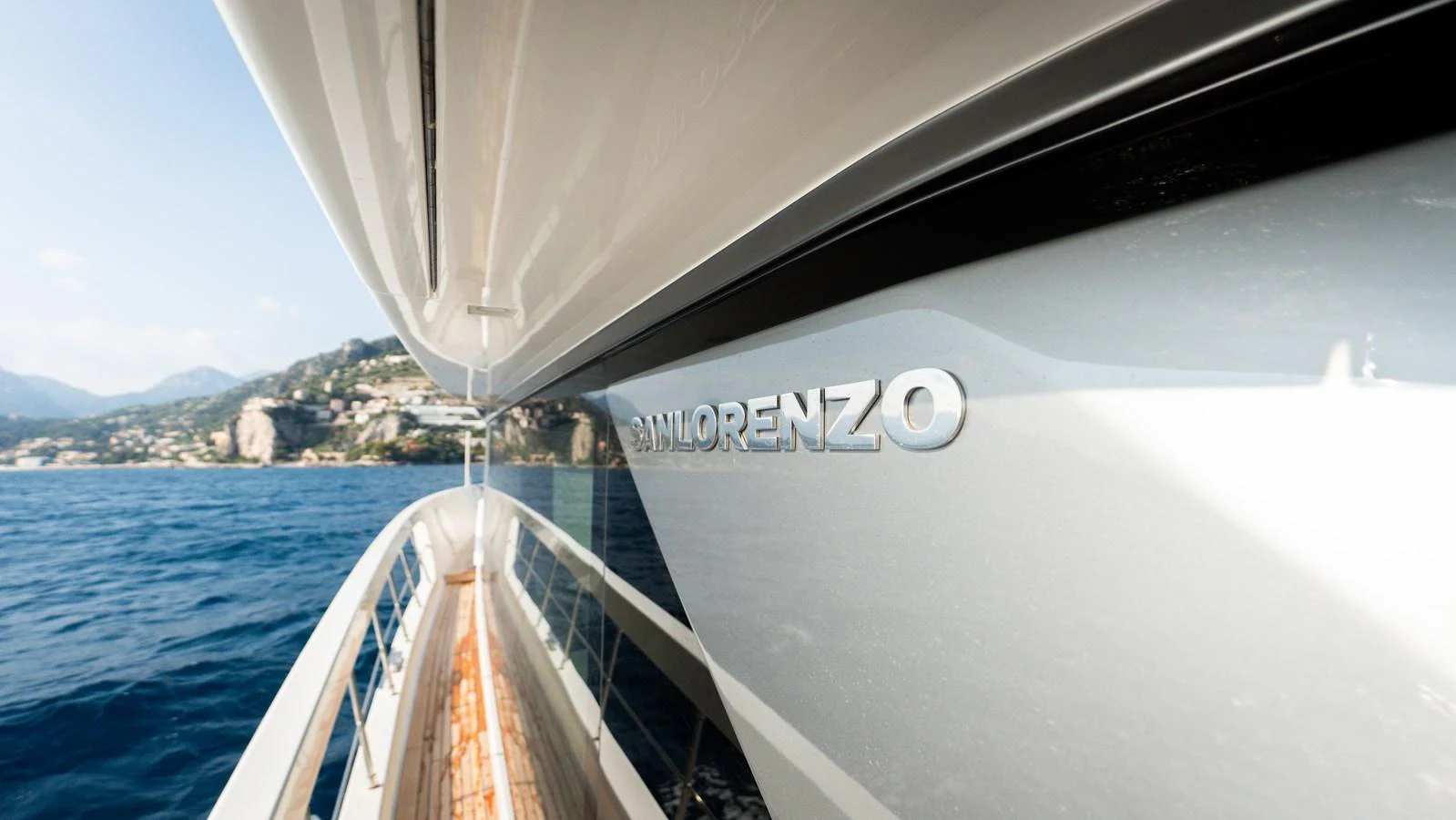 A close-up view of the yacht's sleek exterior with a focus on the brand name and the surrounding scenic coastline. aboard LA Yacht for Sale