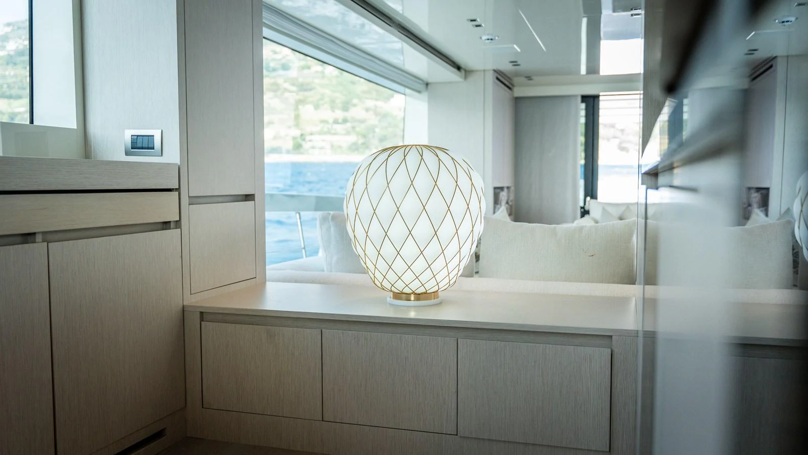 A serene interior space featuring a stylish lamp and large windows offering a view of the water. aboard LA Yacht for Sale