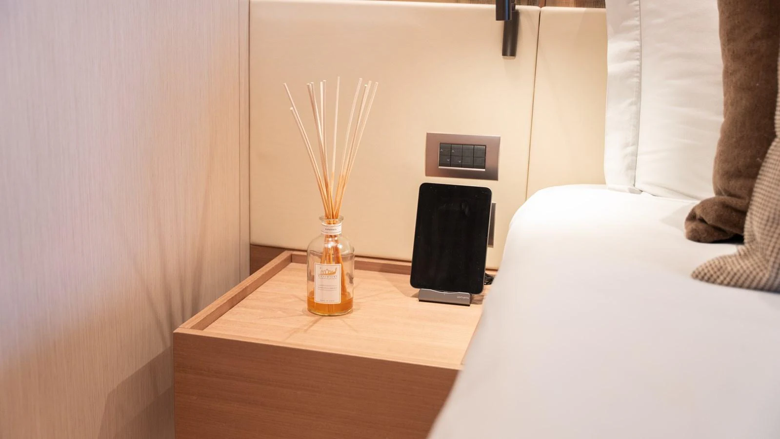 A cozy interior detail featuring a bedside table with a reed diffuser and a tablet stand. aboard LA Yacht for Sale
