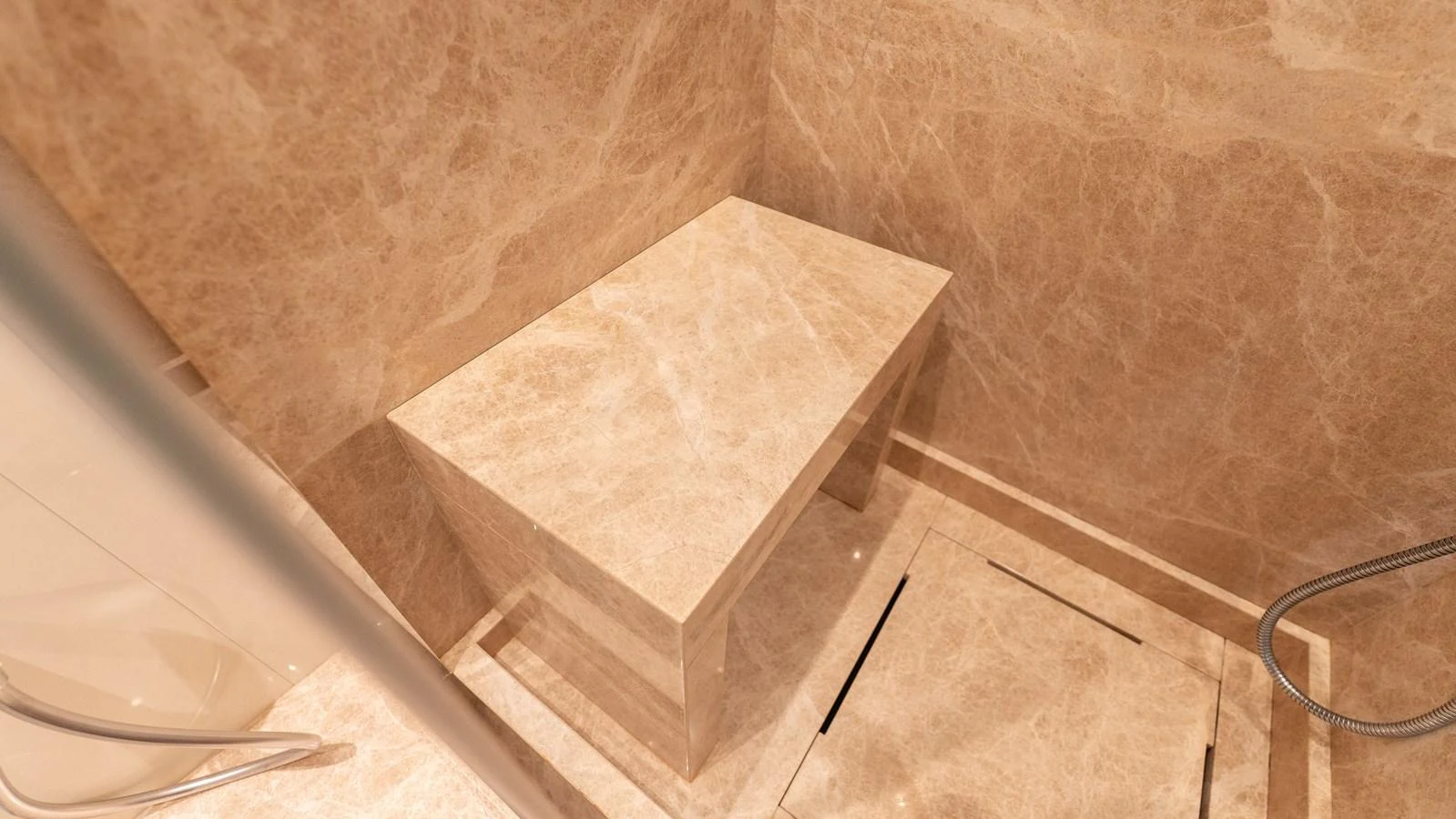 The image showcases a luxurious marble-clad shower area with a built-in bench. aboard LA Yacht for Sale