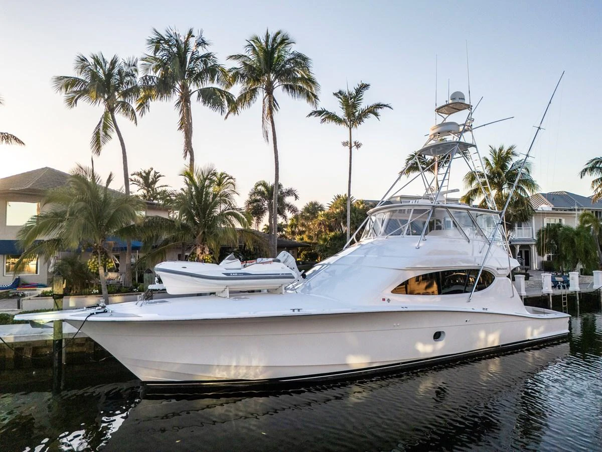 A sleek white yacht is docked in a serene marina surrounded by palm trees. aboard REEL TEXAN Yacht for Sale