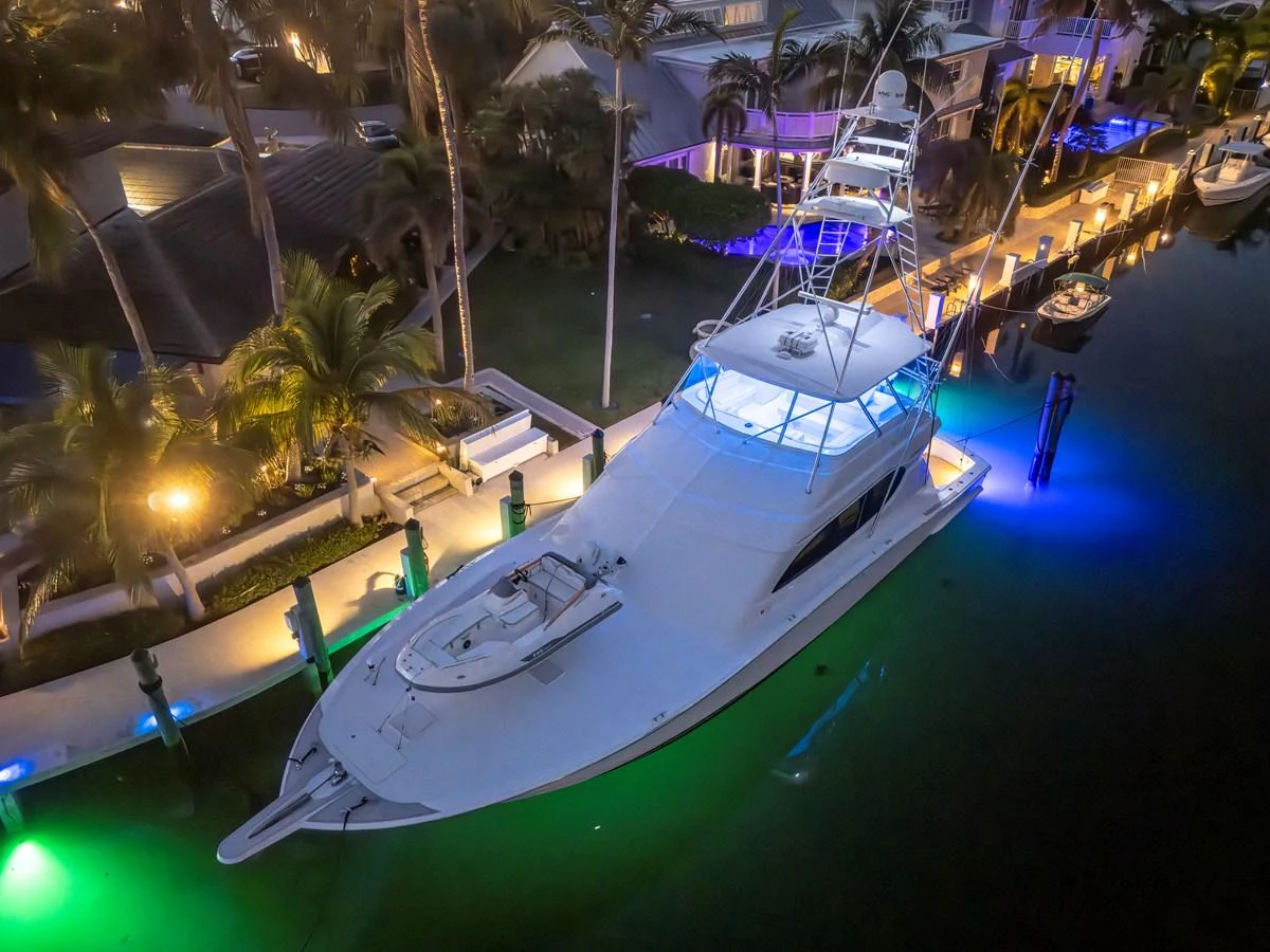 A sleek yacht is docked at night, illuminated by vibrant underwater lights. aboard REEL TEXAN Yacht for Sale