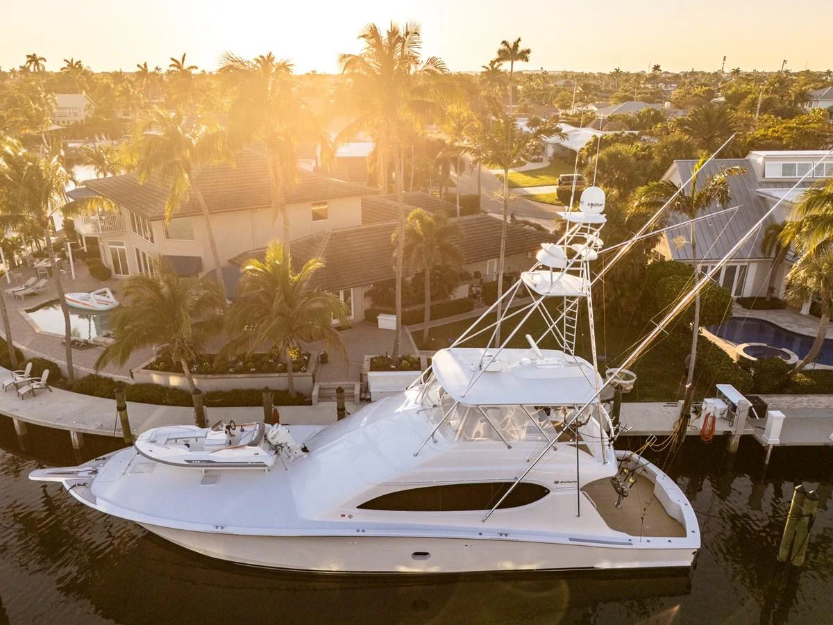 A sleek yacht is docked in a picturesque marina at sunset, surrounded by luxurious waterfront homes. aboard REEL TEXAN Yacht for Sale