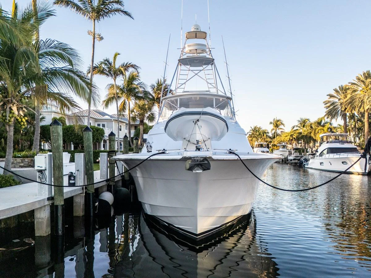 A sleek yacht is docked at a marina surrounded by palm trees and waterfront homes. aboard REEL TEXAN Yacht for Sale