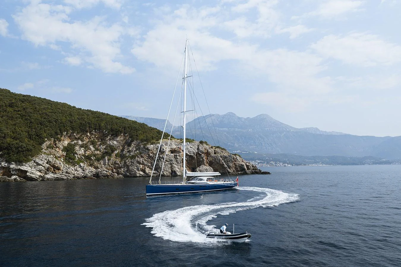 A sleek yacht sails along a picturesque coastline, accompanied by a tender creating a dynamic wake. aboard FARFALLA Yacht for Sale