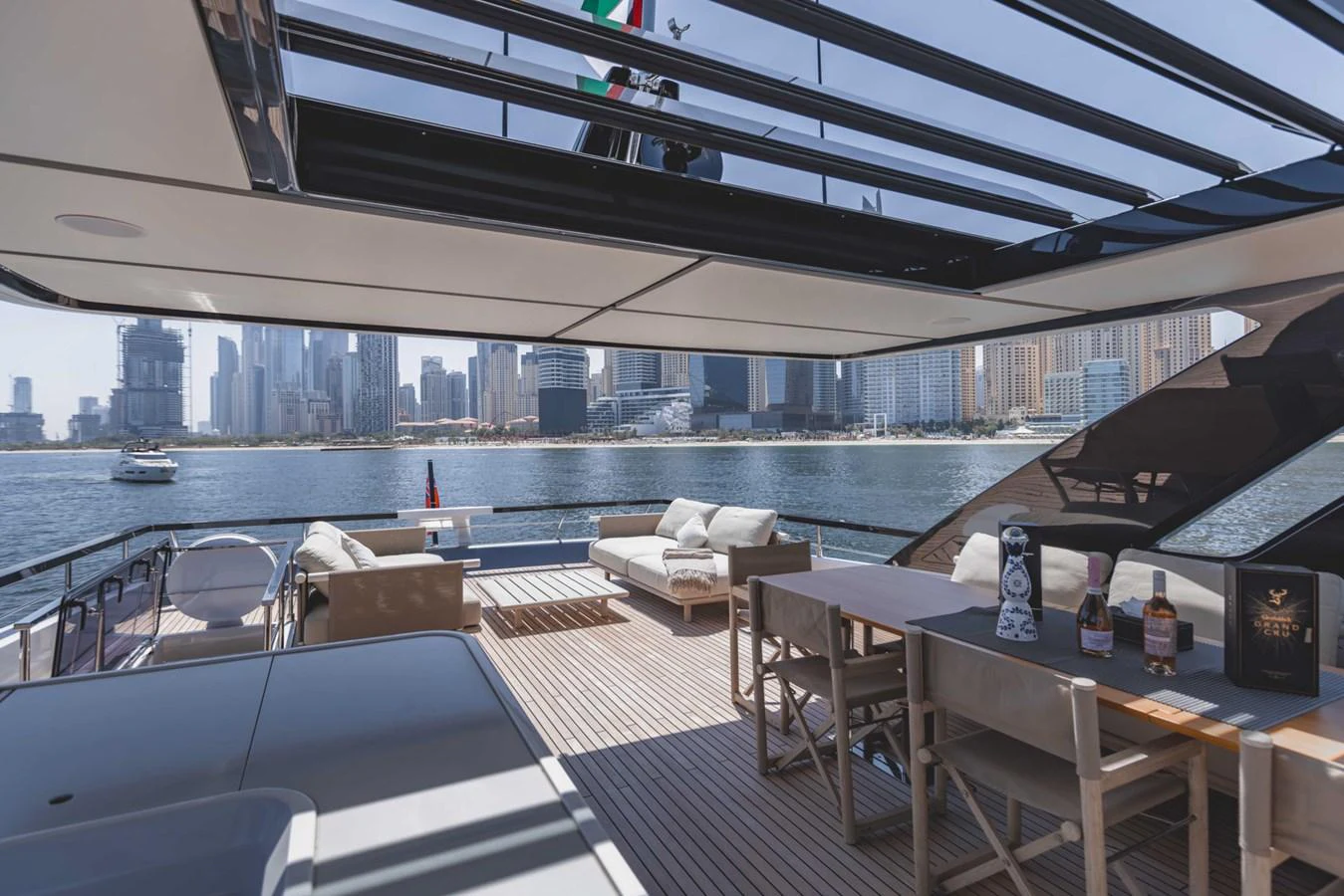 The aft deck offers a luxurious outdoor living space with comfortable seating and a dining area, overlooking a stunning city skyline. aboard CYRUS Yacht for Sale