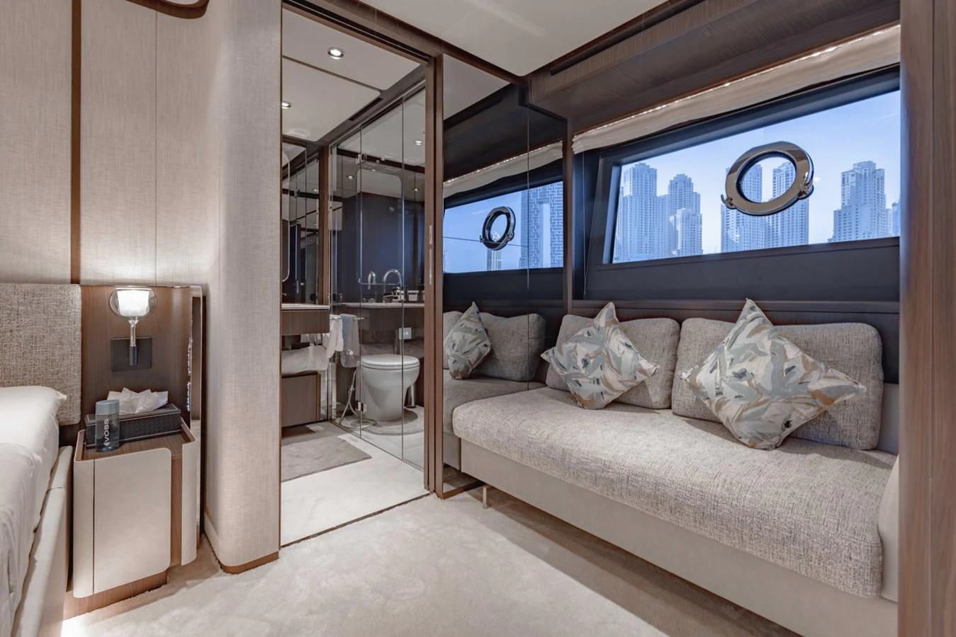 The stateroom features a plush sofa, elegant decor, and a view of the city skyline through large windows. aboard CYRUS Yacht for Sale