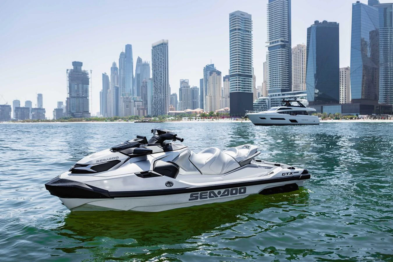 A sleek Sea-Doo jet ski floats on calm waters with a city skyline in the background. aboard CYRUS Yacht for Sale