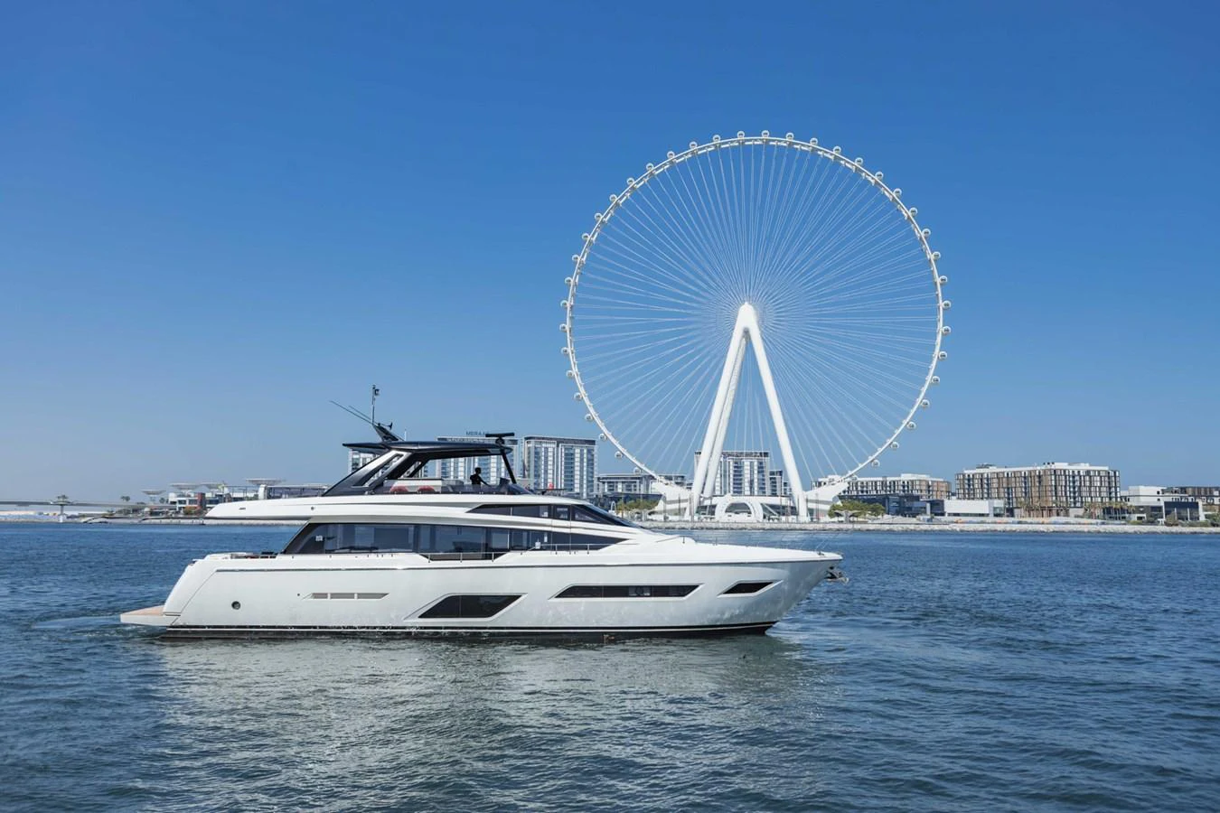 A sleek, modern yacht cruises on calm waters with a large Ferris wheel in the background. aboard BELLA III Yacht for Sale