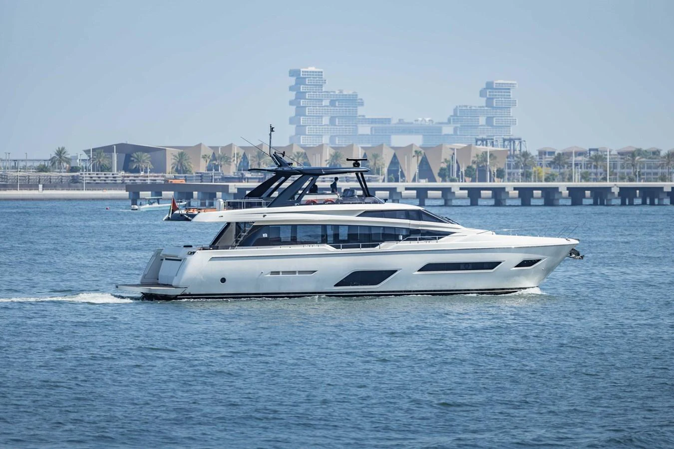 A sleek and modern yacht cruises gracefully on calm waters with a cityscape in the background. aboard BELLA III Yacht for Sale