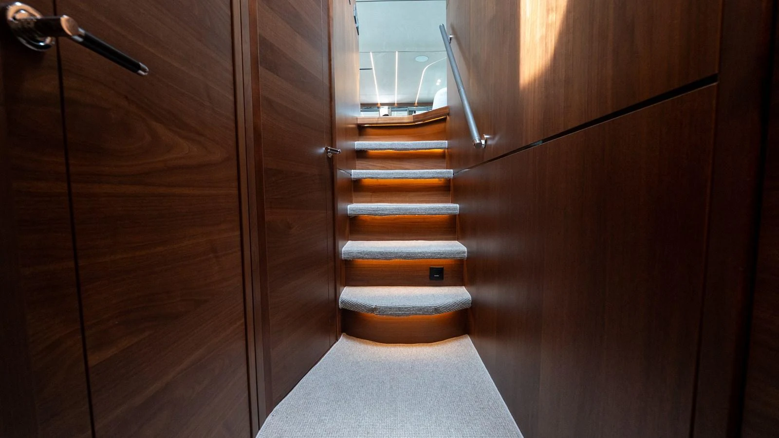 A beautifully crafted wooden staircase with soft lighting leads to the upper deck. aboard PARAGON Yacht for Sale