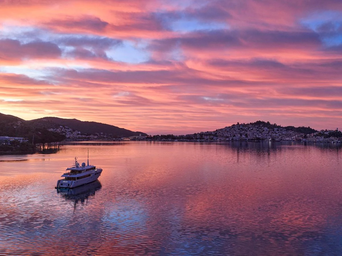 A luxurious yacht is anchored in a serene bay under a breathtaking sunset sky. aboard ULYSSES Yacht for Sale