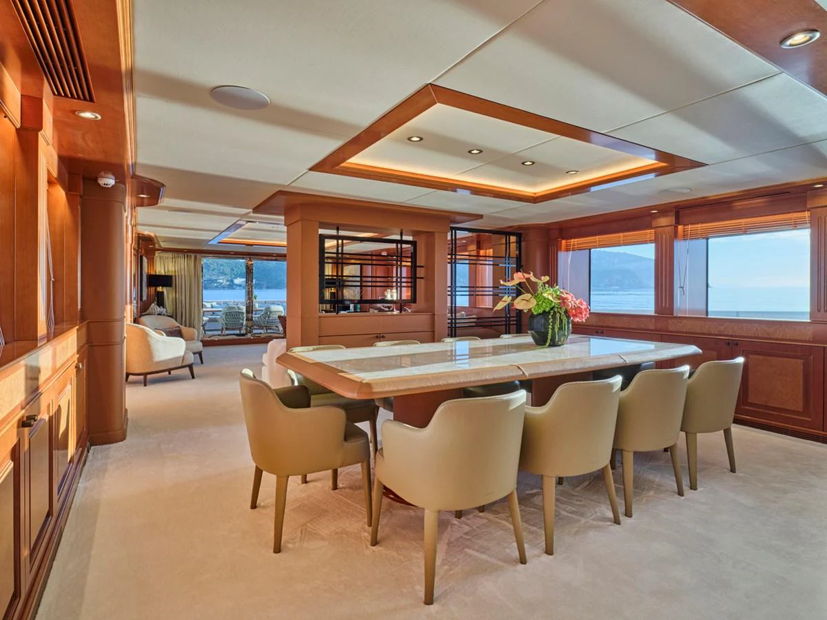 The yacht's dining area features a large table surrounded by comfortable chairs, with ample natural light and elegant wooden accents. aboard ULYSSES Yacht for Sale