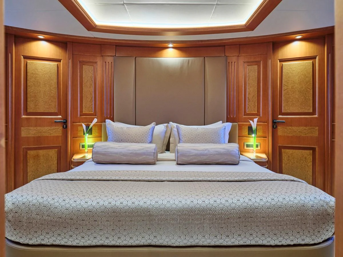 The master stateroom features a luxurious bed with elegant wood paneling and ambient lighting. aboard ULYSSES Yacht for Sale