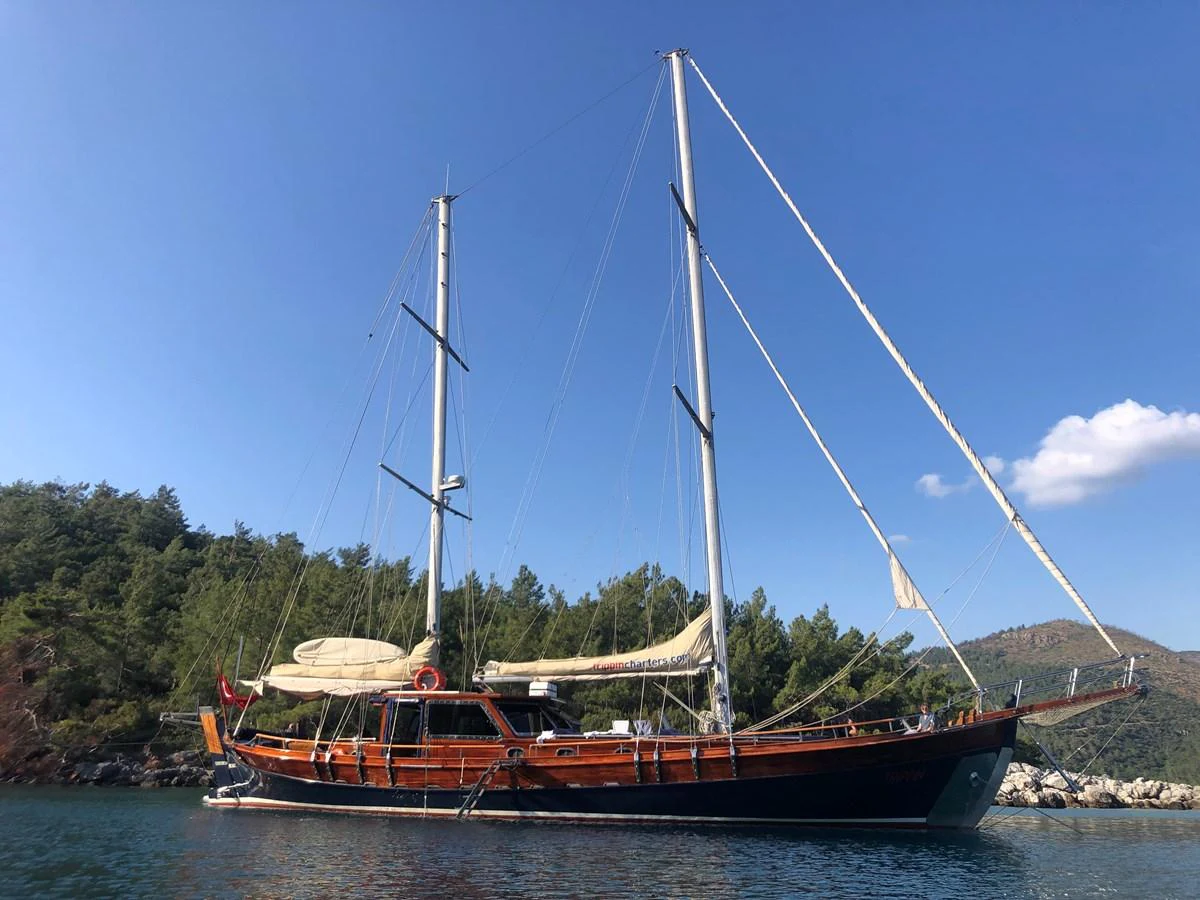 A classic sailing yacht anchored in a serene bay with lush greenery in the background. aboard TRIPPIN Yacht for Sale