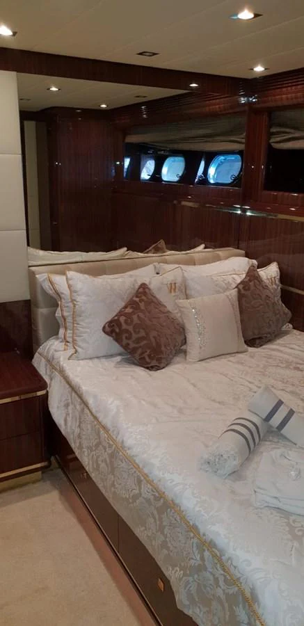 The stateroom features a luxurious bed with elegant bedding and plush pillows, complemented by rich wood paneling and ample natural light from the windows. aboard LEOPARD 105 FT Yacht for Sale