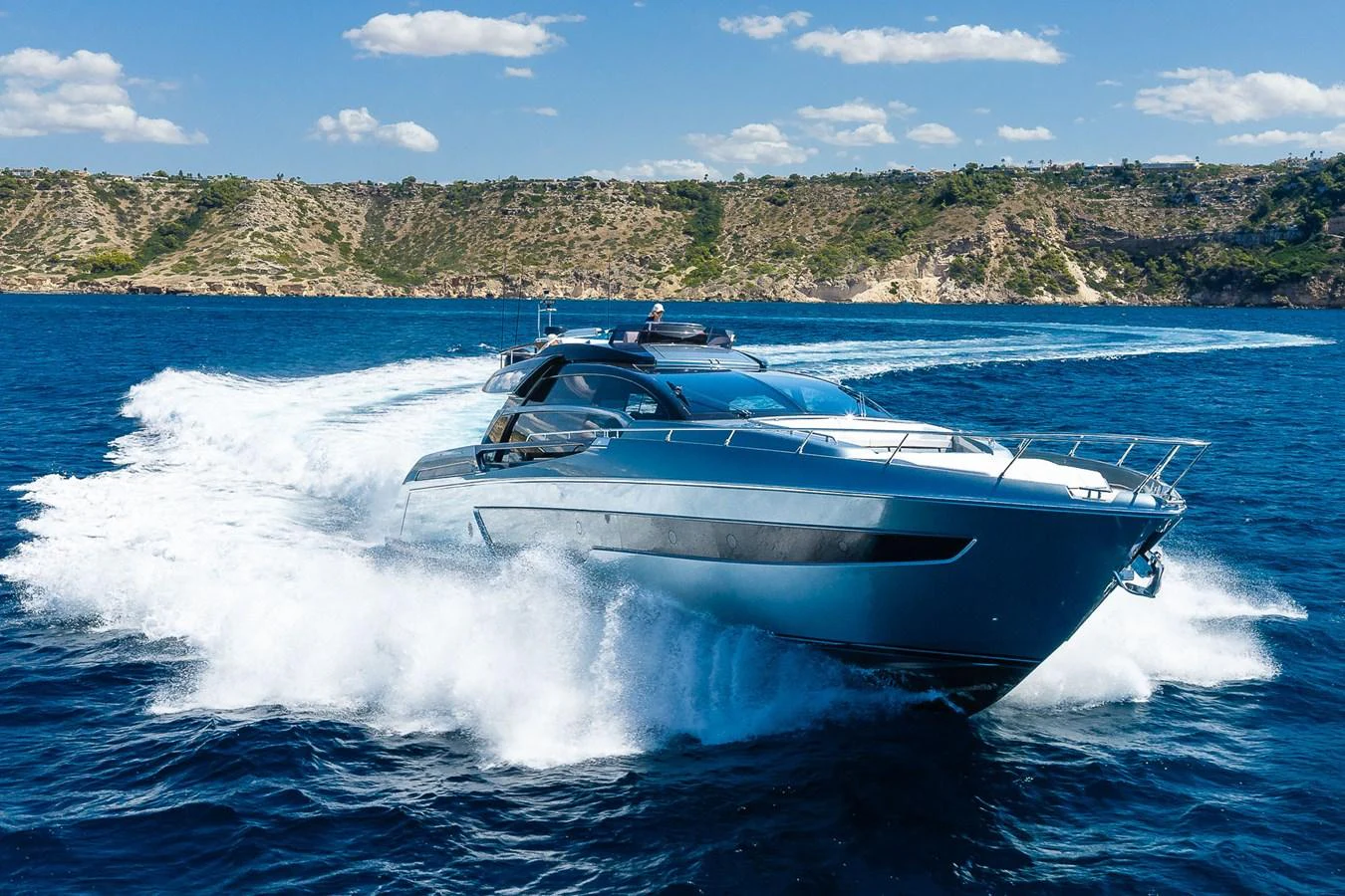 A sleek yacht cruises swiftly through vibrant blue waters against a scenic coastal backdrop. aboard ACQUA Yacht for Sale