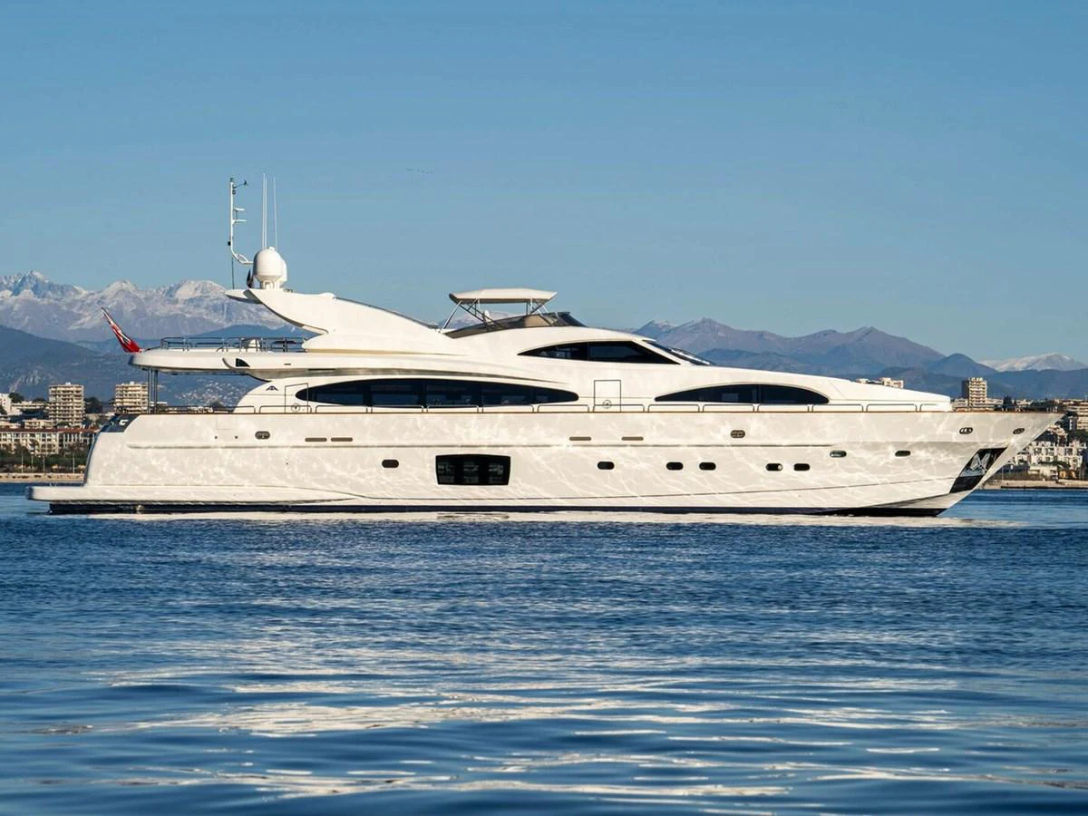 A sleek and modern yacht glides gracefully on calm waters with a stunning cityscape and mountains in the background. aboard SPRING TIDE Yacht for Sale
