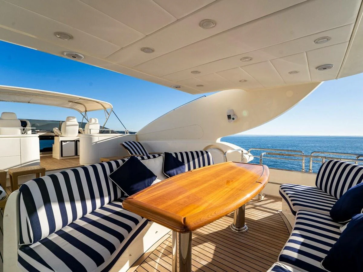 The aft deck offers a luxurious outdoor dining area with striped seating and a polished wooden table, perfect for enjoying meals with a sea view. aboard SPRING TIDE Yacht for Sale
