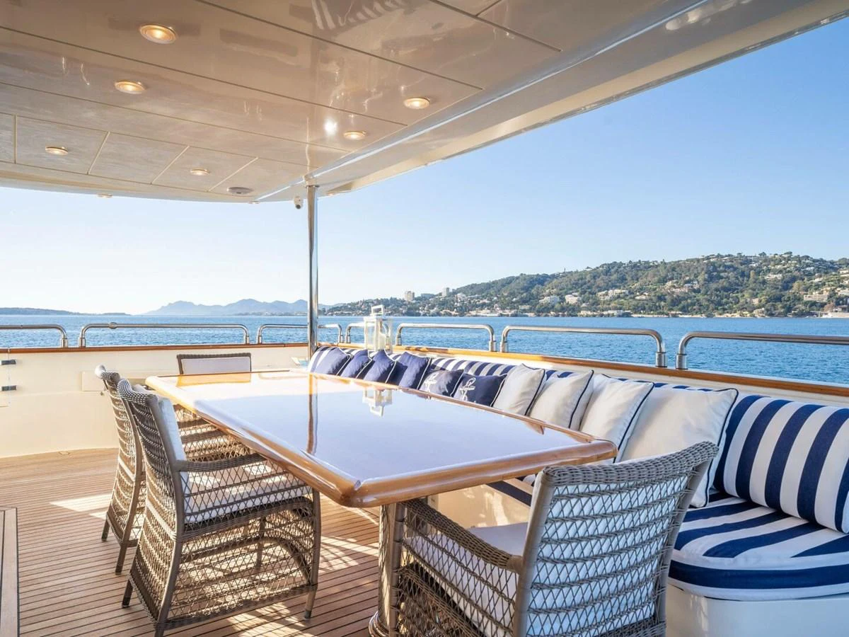 The aft deck features a spacious dining area with a polished wooden table and comfortable wicker chairs, offering stunning views of the surrounding waters. aboard SPRING TIDE Yacht for Sale