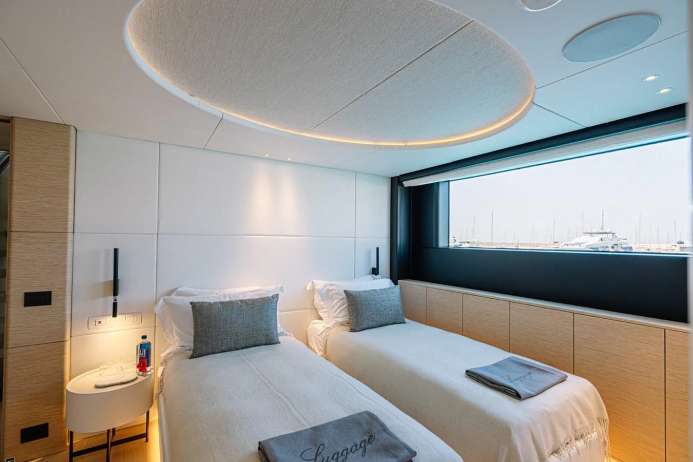 A serene twin stateroom with modern furnishings and a large window offering a marina view. aboard RAISA Yacht for Sale