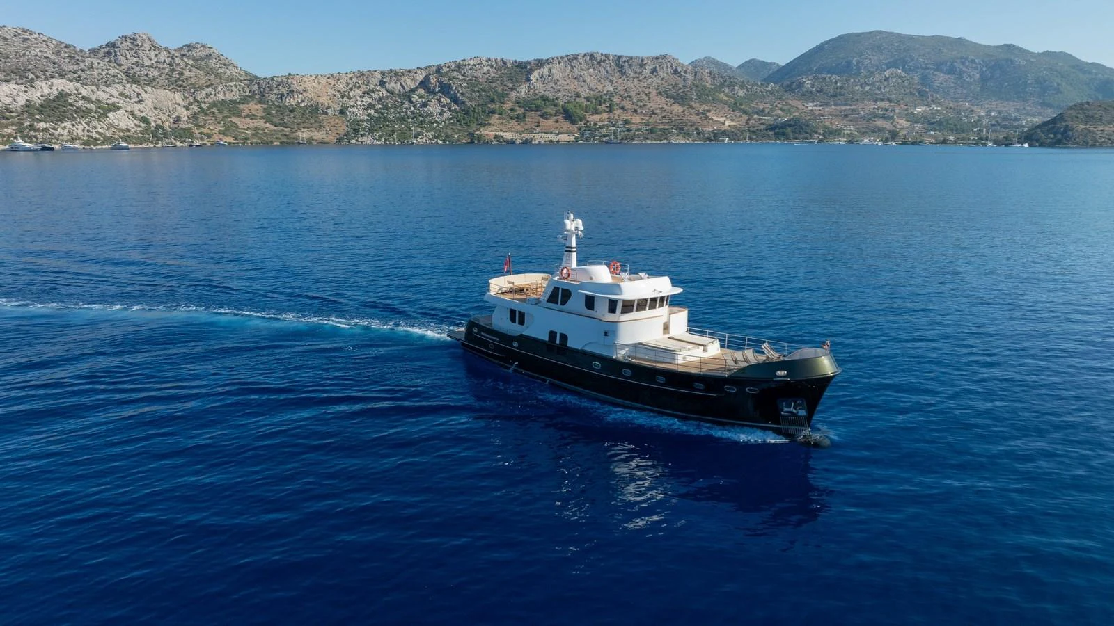 A sleek yacht cruises through calm blue waters with a scenic mountainous backdrop. aboard TROYWIZARD Yacht for Sale