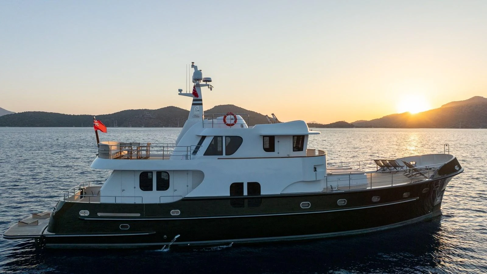 A classic yacht cruising at sunset with serene waters and distant hills in the background. aboard TROYWIZARD Yacht for Sale