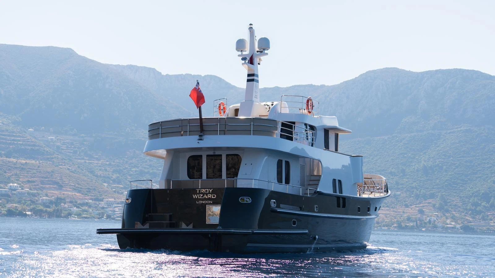 A luxurious yacht is anchored in calm waters with scenic mountains in the background. aboard TROYWIZARD Yacht for Sale