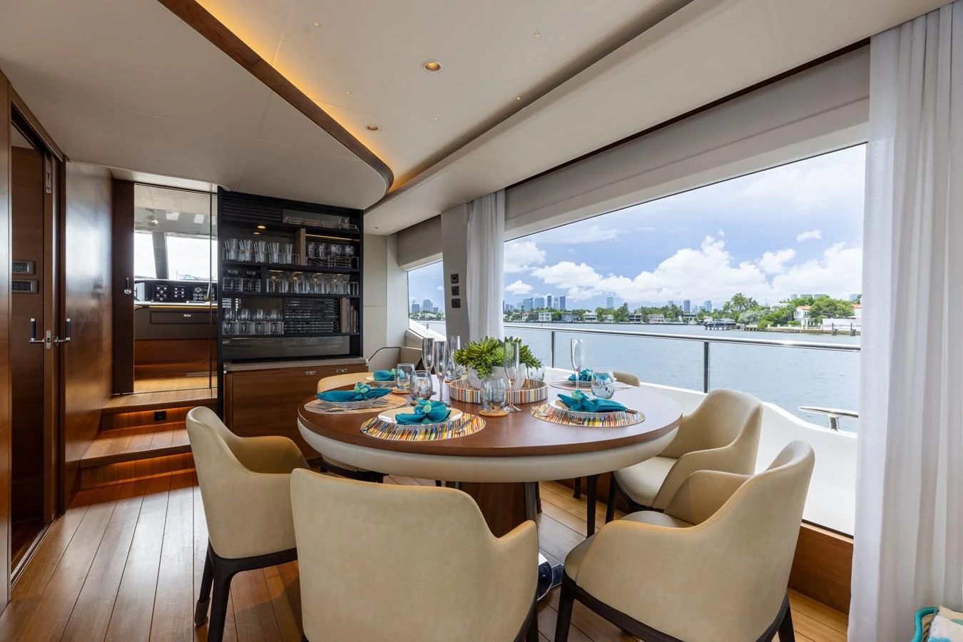 The yacht's dining area offers a luxurious setting with a round table and comfortable seating, complemented by large windows providing a scenic view. aboard TOMORROW NEVER KNOWS Yacht for Sale
