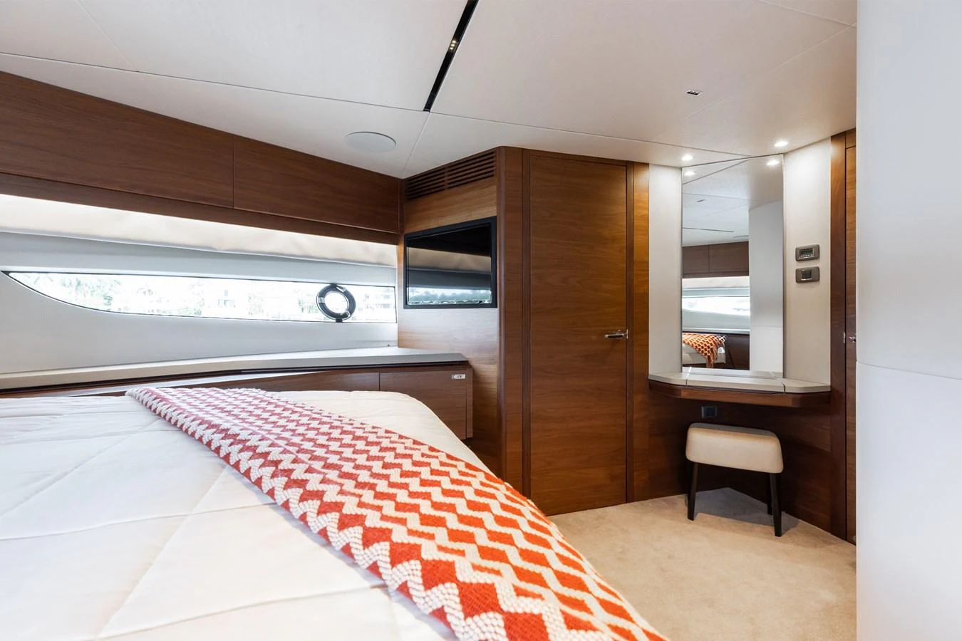 The stateroom features a cozy bed with a stylish patterned throw and a vanity area with a mirror and stool. aboard TOMORROW NEVER KNOWS Yacht for Sale